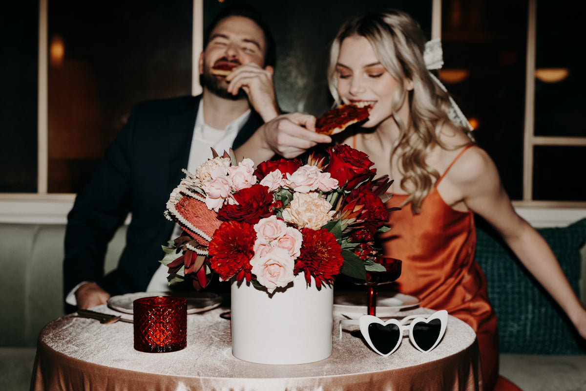Couple enjoying Valentine’s dinner with a red and blush floral centerpiece by Flowers for Dreams.