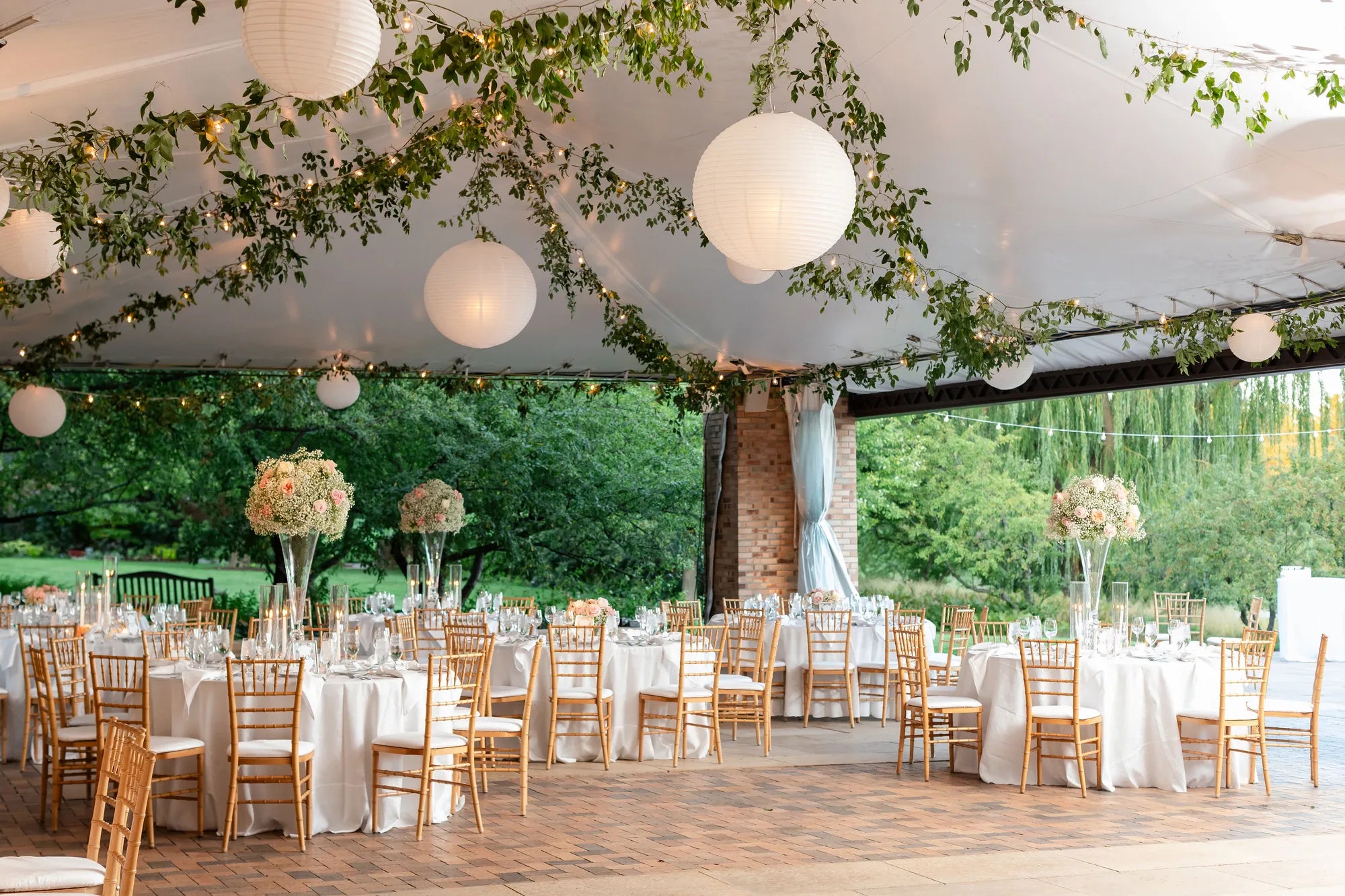 Elegant outdoor wedding reception with greenery, lanterns, and floral centerpieces on tables by Flowers for Dreams.