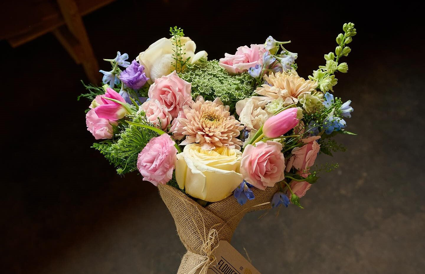 Hand holding a fresh spring bouquet wrapped in burlap with Flowers for Dreams tag.