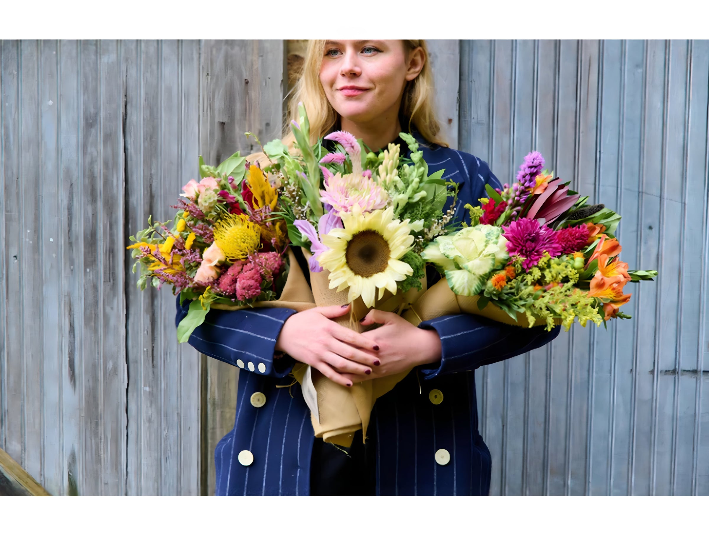 Woman holding three vibrant Flowers for Dreams bouquets with sunflowers, proteas, and assorted wildflowers.