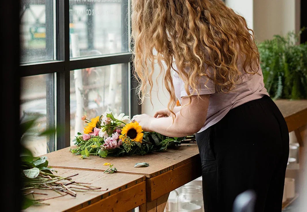 Woman arranging fresh wedding flowers and bridal bouquet stems inside the Flowers for Dreams floral studio.