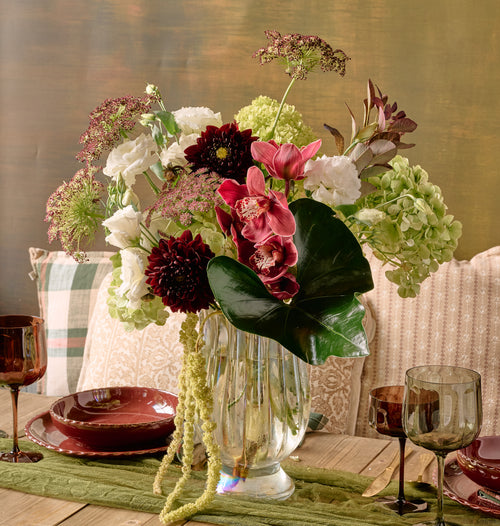 Bordeaux floral arrangement of deep burgundy dahlias, dark red roses, chocolate cosmos, and amaranth in a crystal vase on dark dramatic background