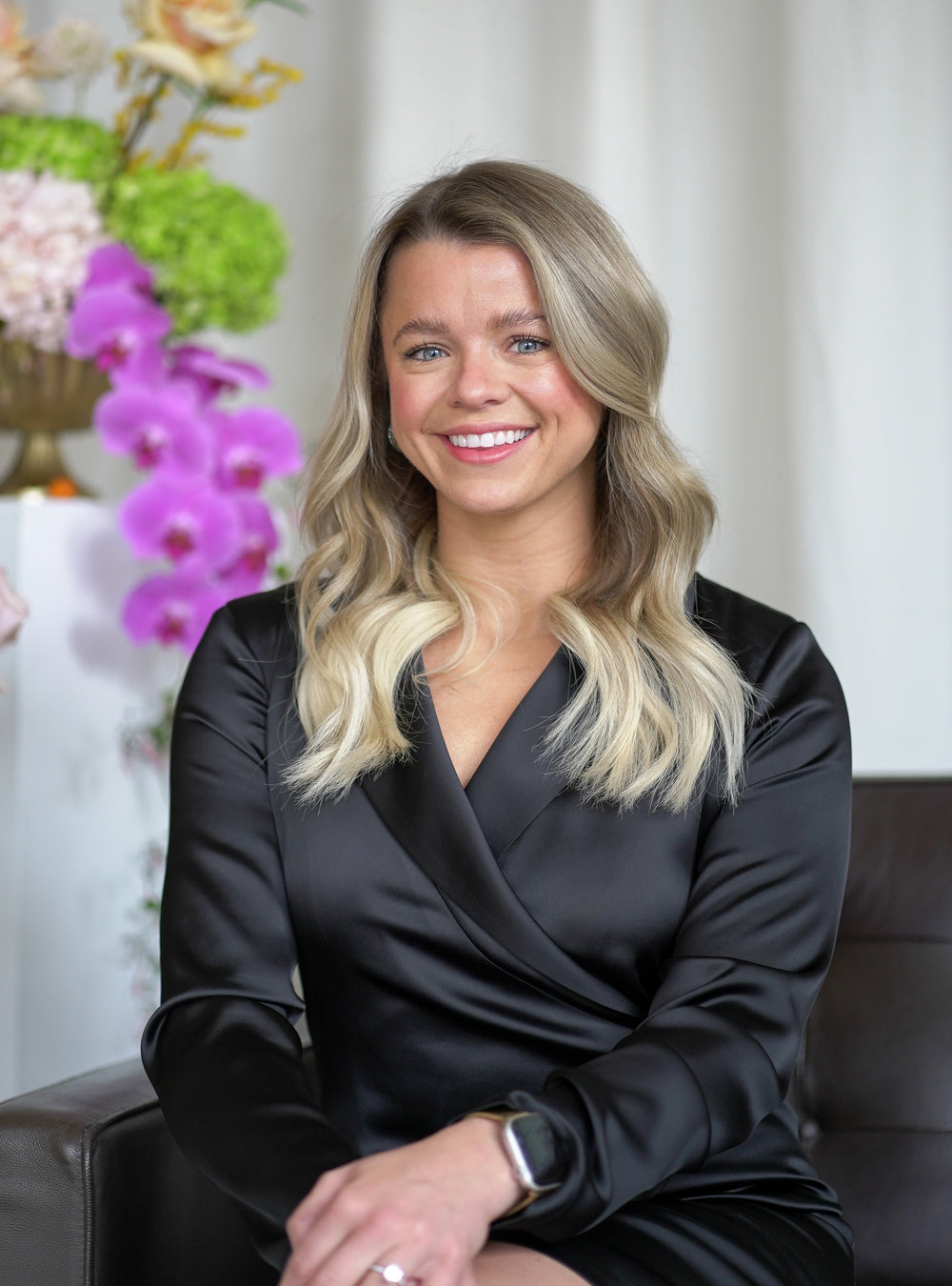 Woman in a black outfit sitting in a room with flowers in the background