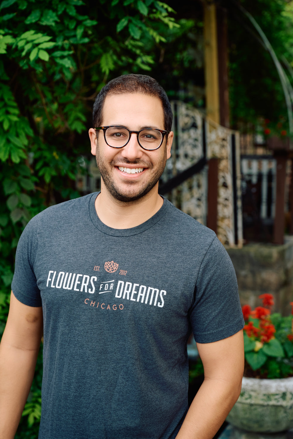 Man wearing a 'Flowers for Dreams Chicago' t-shirt in an outdoor setting with plants.