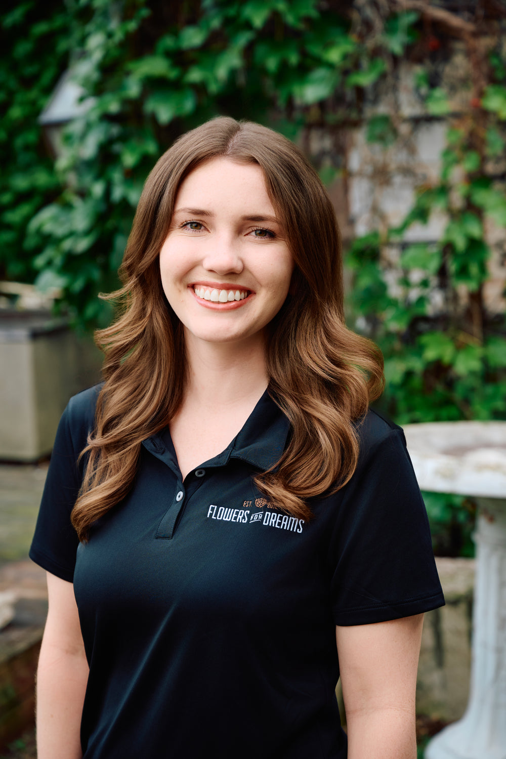 Woman wearing a black polo shirt with 'Flowers of Dreams' logo outdoors.
