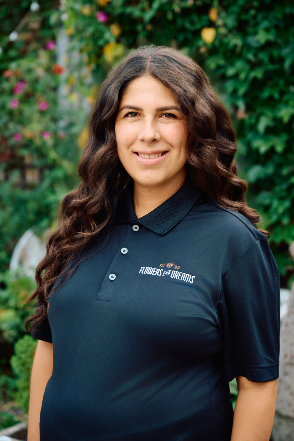 Woman wearing a black polo shirt with a logo in front of green foliage