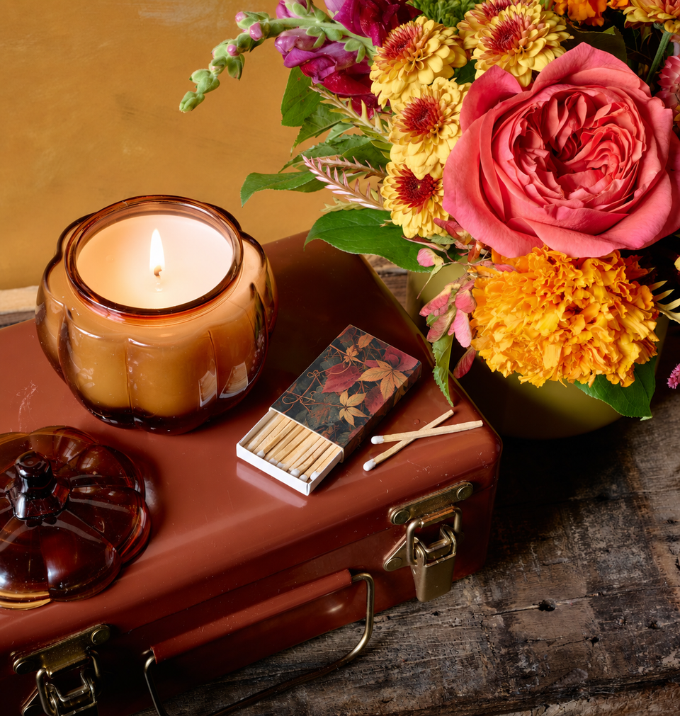 Flowers for Dreams fall gift set with amber ribbed candle, matchbox, and autumn floral arrangement on vintage suitcase