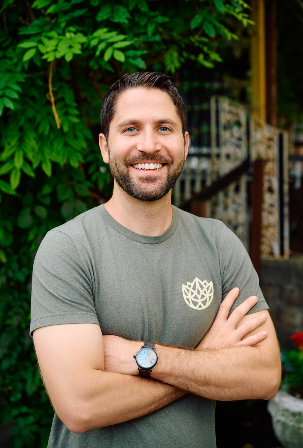 Man wearing a green t-shirt with a logo, standing outdoors with greenery in the background
