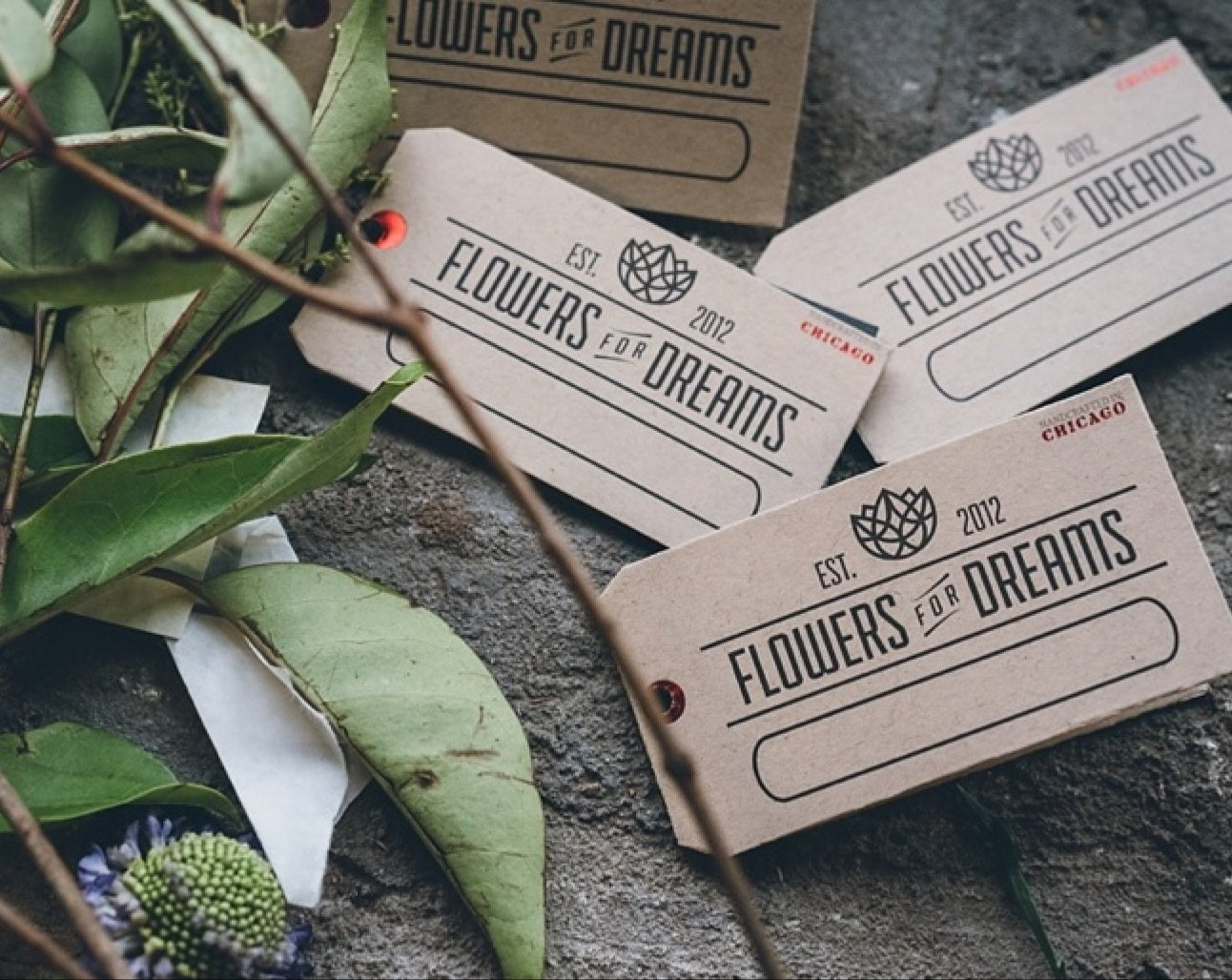 Flowers for Dreams branded tags on a stone surface with greenery.